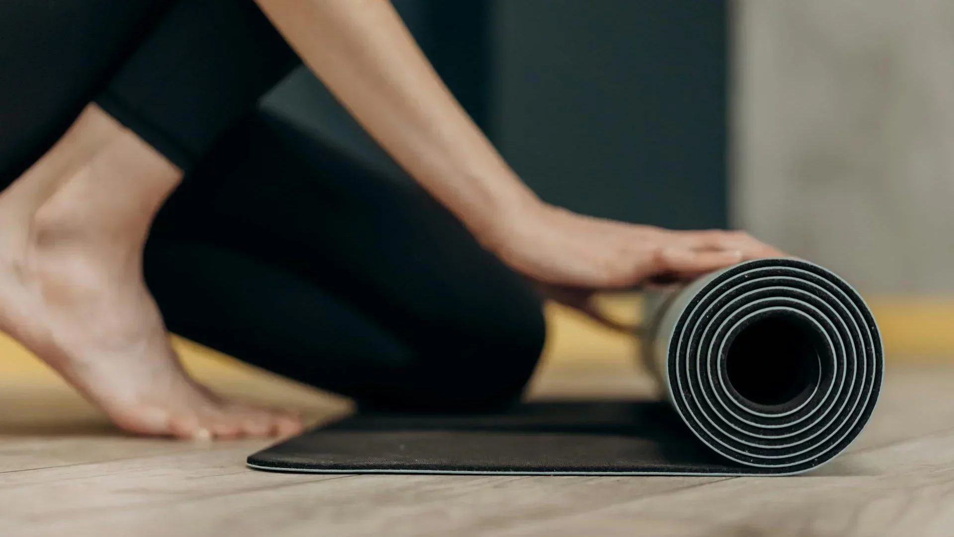 Person rolling out a yoga mat on studio floor — symbolizing preparation, routine, and yoga class scheduling.