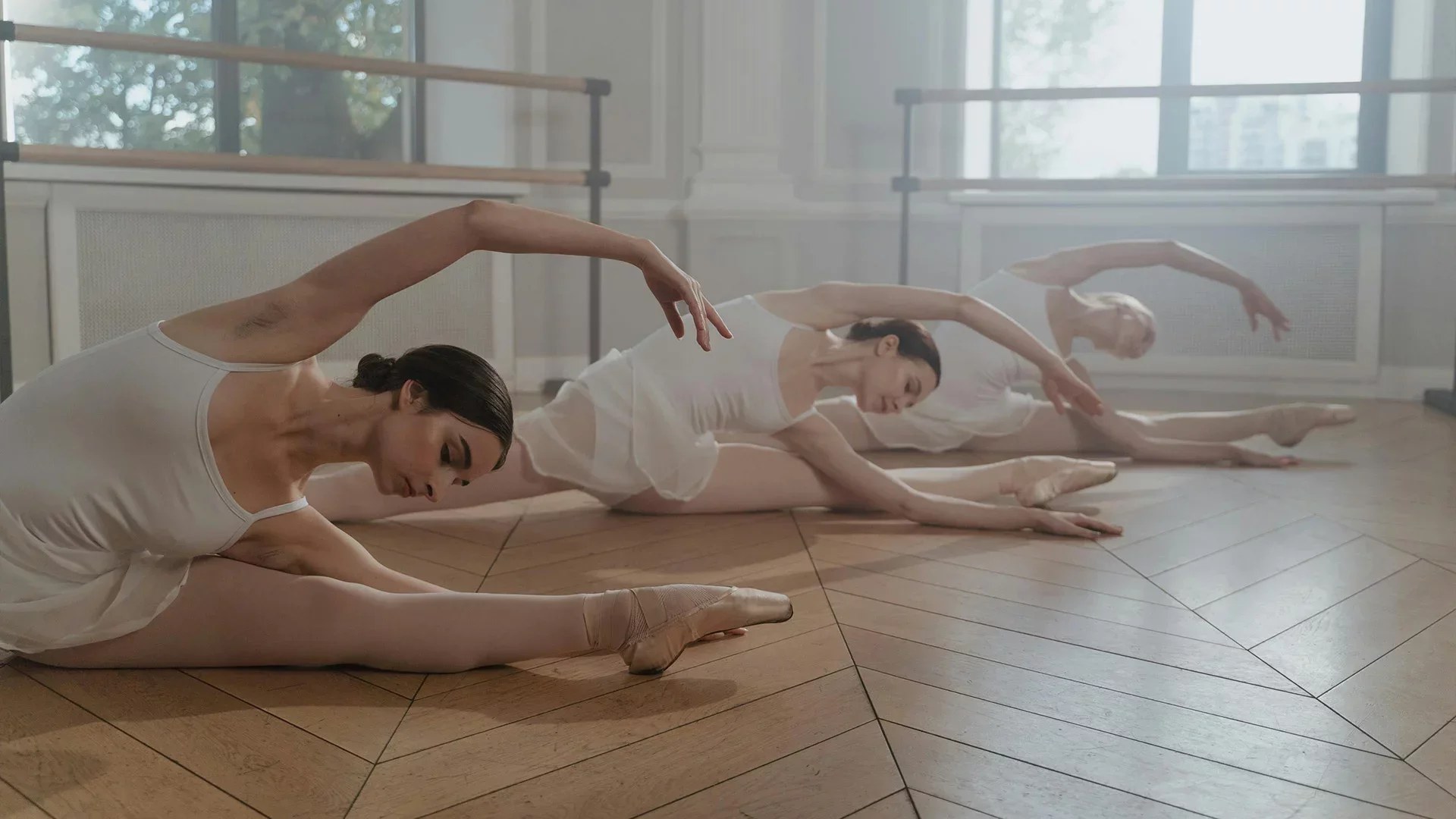 Three ballet dancers stretching in a studio during class—ideal visual for dance studio memberships and recurring class bookings